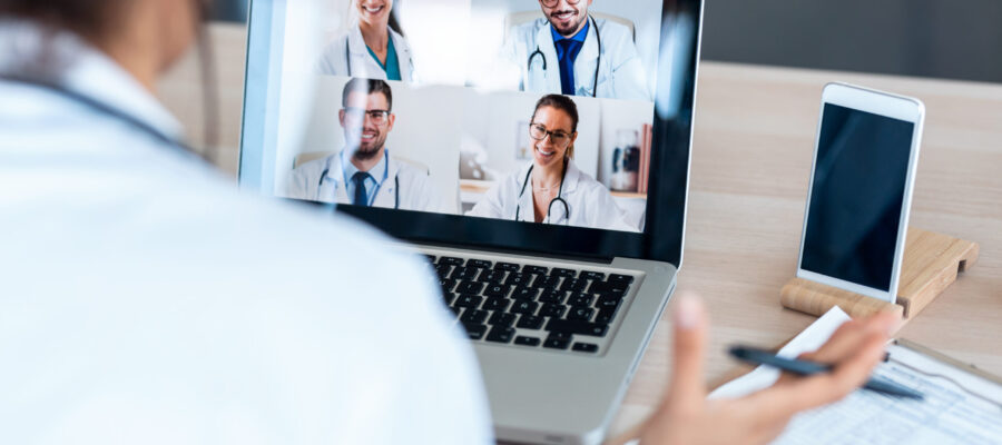 Back view of female doctor talking with colleagues through a video call with a laptop in the consultation.